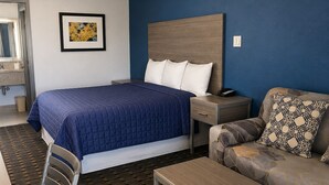 Ein Hotelzimmer mit Bett, Sofa, Sessel, Tisch, Nachttisch und einem Gemälde an der Wand.
