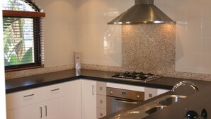 Una cuina moderna amb armaris blancs, una campana extractora d'acer inoxidable, una cuina a gas i un forn integrat.