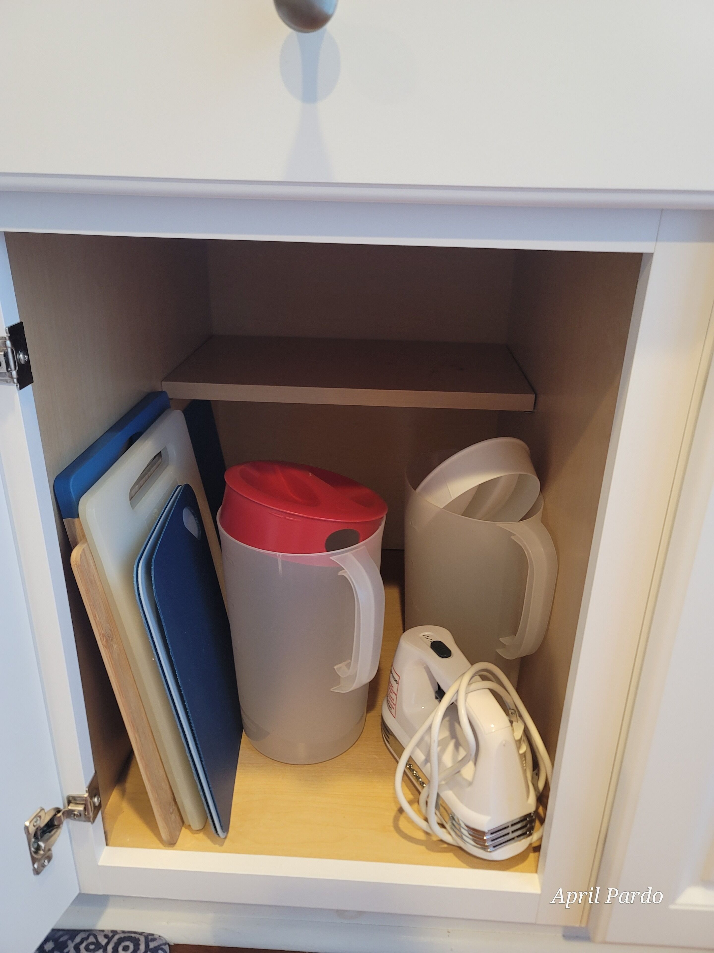 Un compartimento con una carpeta azul, una taza rojo y blanco, una tetera eléctrica blanca y un secador de pelo blanco.