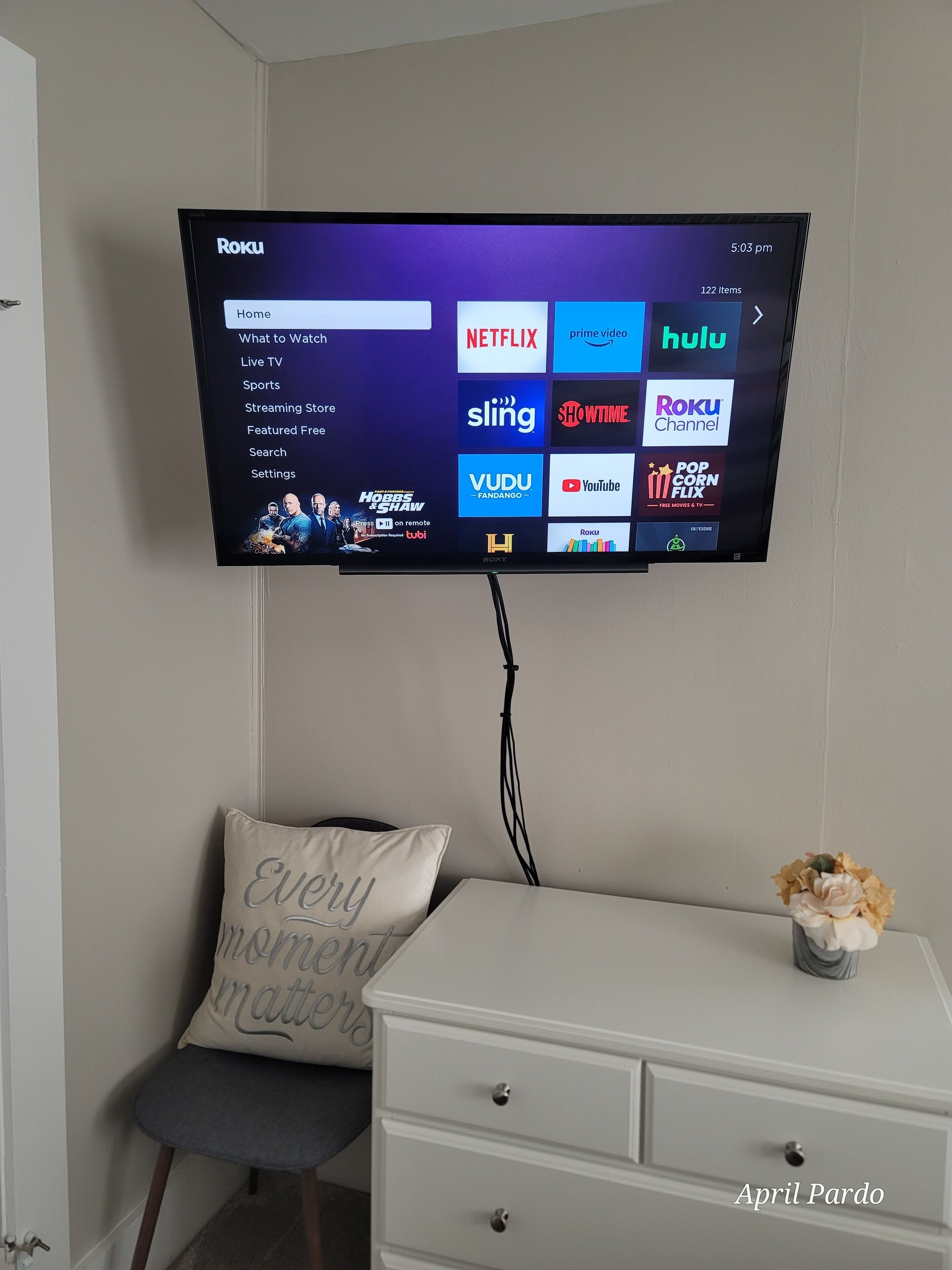 Un téléviseur à écran plat fixé au mur affiche l’interface Roku, qui donne accès à divers services de diffusion en continu.