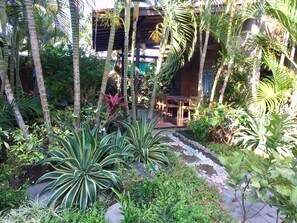 Stroll through a serene garden oasis with lush palm trees and broad-leafed plants, surrounded by a tranquil patio area with seating.