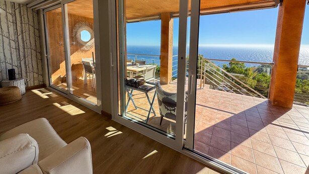 Een ruime kamer met grote schuifglazen deuren die uitkomen op een terras met uitzicht op de oceaan.