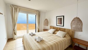Een hotelkamer met een groot bed, uitzicht op het strand en een geweven lamp.