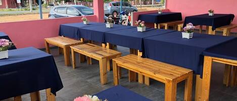 A covered outdoor seating area with tables and benches, some with flowers.
