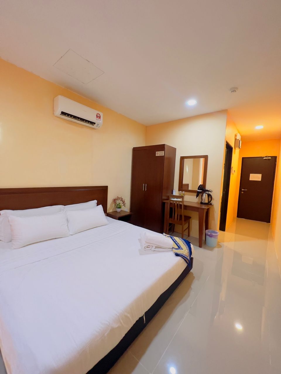 A hotel room with a bed, a desk, a wardrobe, and an air conditioning unit.