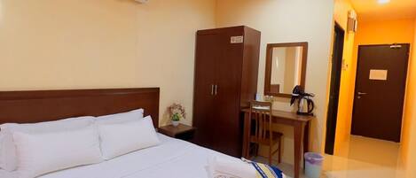A hotel room with a bed, a desk, a wardrobe, and an air conditioning unit.