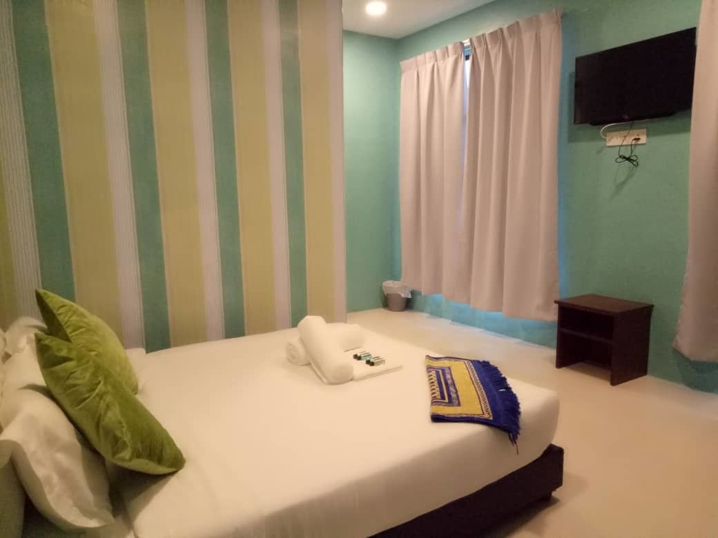 Un lit bien fait, avec des oreillers et une couverture, une petite table de chevet et un téléviseur fixé au mur.