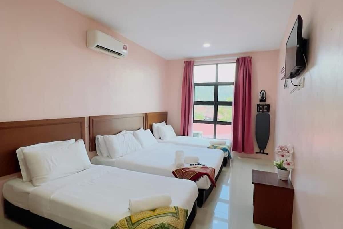 Una habitación de hotel con tres camas, un equipo de aire acondicionado, un televisor y una ventana con cortinas.