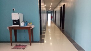 Un pasillo de hotel con un dispensador de agua, una mesa con un cuenco y servilletas, y un tapete estampado en el suelo.
