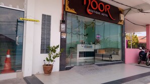 Entrada de un hotel boutique con fachada de vidrio, una recepción y una planta en maceta.