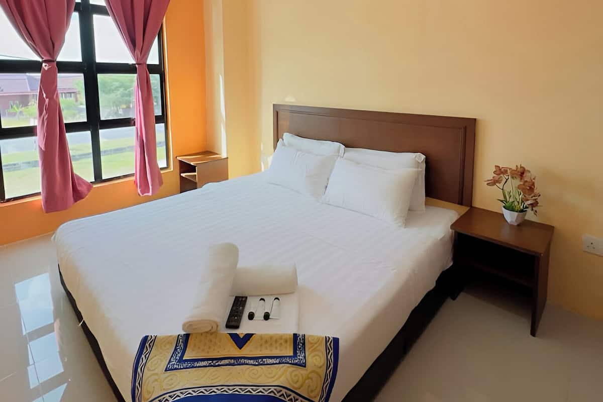 Una habitación de hotel con una cama grande, un cabecero de madera, una mesita de noche con un jarrón de flores y un equipo de aire acondicionado en la pared.