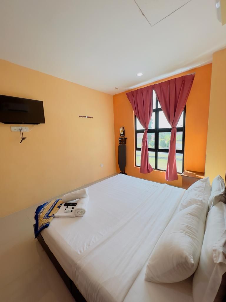 Habitación de hotel con cama, televisor de pantalla plana montado en la pared, ventana con cortinas y un reloj en la mesita de noche.