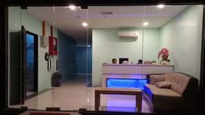 Un área de recepción moderna con entrada de vidrio, un mostrador de recepción, un sofá y una pequeña mesa.