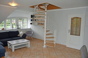 Un amplio salón con una escalera en espiral, un sofá, una mesa de centro y vistas al exterior a través de grandes ventanales.