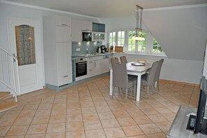 Una cocina moderna con armarios blancos, una mesa de comedor con sillas y un amplio ventanal que proporciona luz natural.