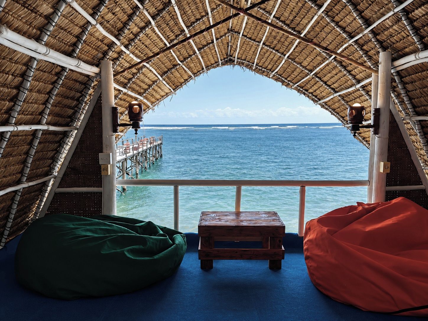 Una habitación con techo de paja, un banco de madera y vista al océano.