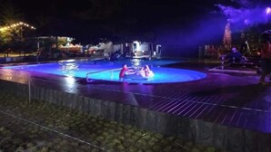 Een zwembad in de vorm van een cirkel, omgeven door een houten terras en een lage stenen muur, 's nachts verlicht.