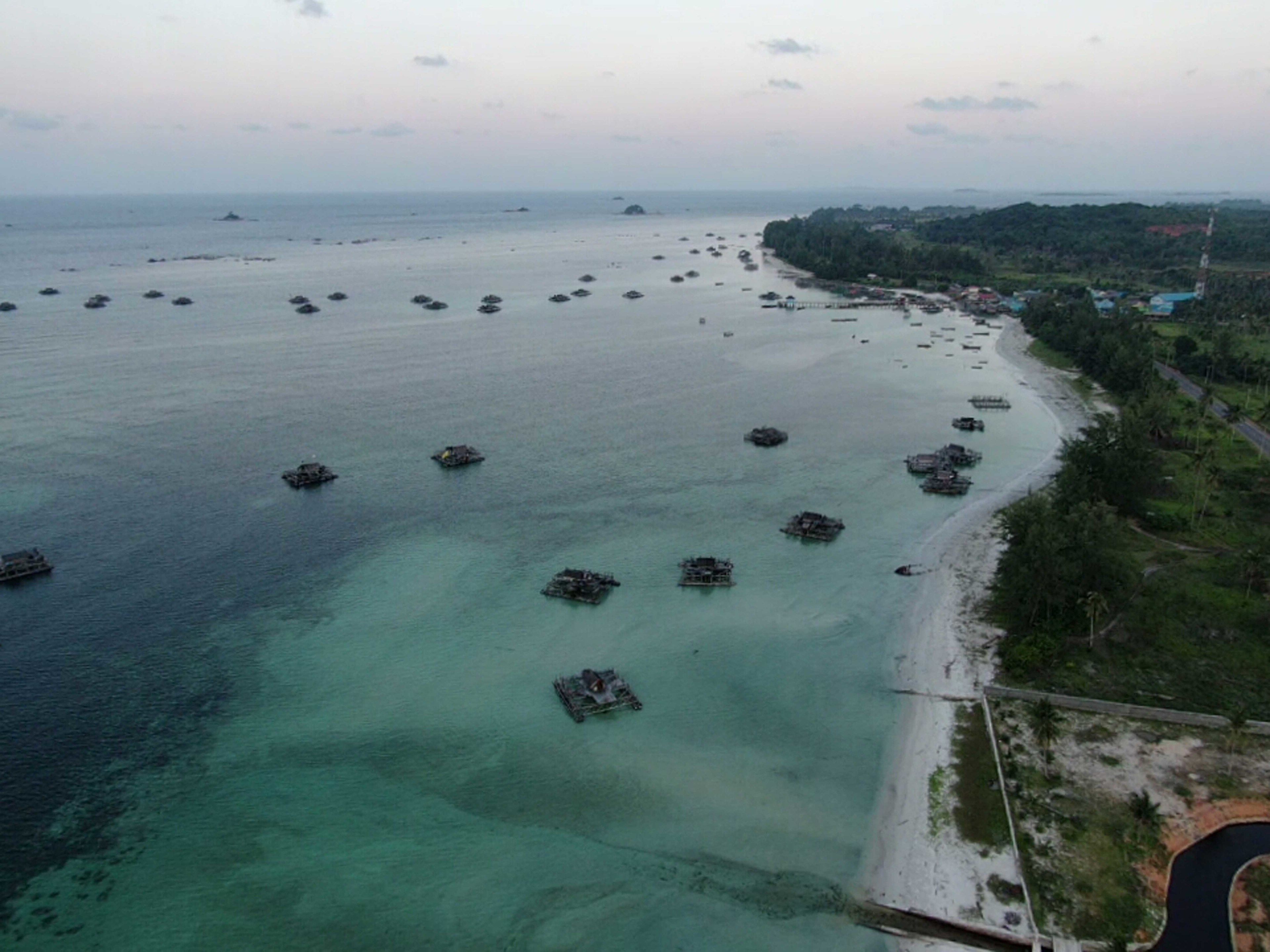 An aerial view of a coastal area with numerous boats anchored in the water, a sandy beach, and a road running parallel to the shore.