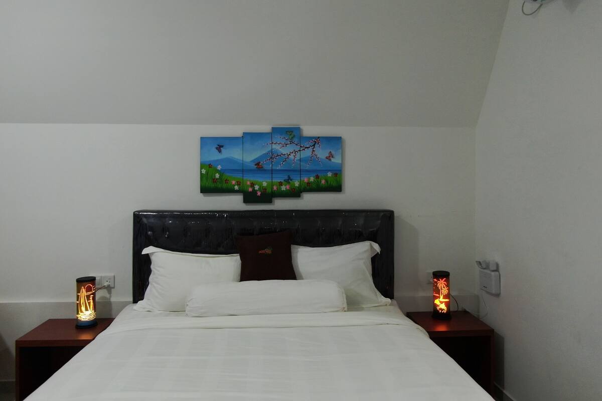Ein ordentlich bezogenes Bett mit weißen Leinen, einem dunklen Kopfteil und einem Wandbild, das eine Landschaft mit Vögeln und Blumen zeigt.