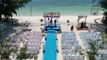 A beach wedding ceremony with a blue aisle, white chairs, and a floral arch.