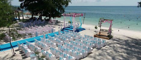 Decoración de boda en la playa con filas de sillas y un escenario.