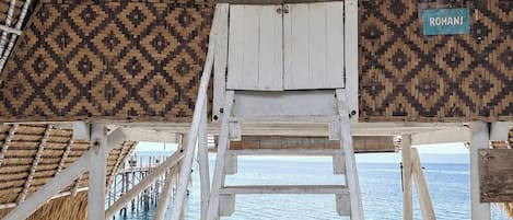 A wooden deck with a thatched roof, a sign reading 'ROHANI', and a view of the sea.