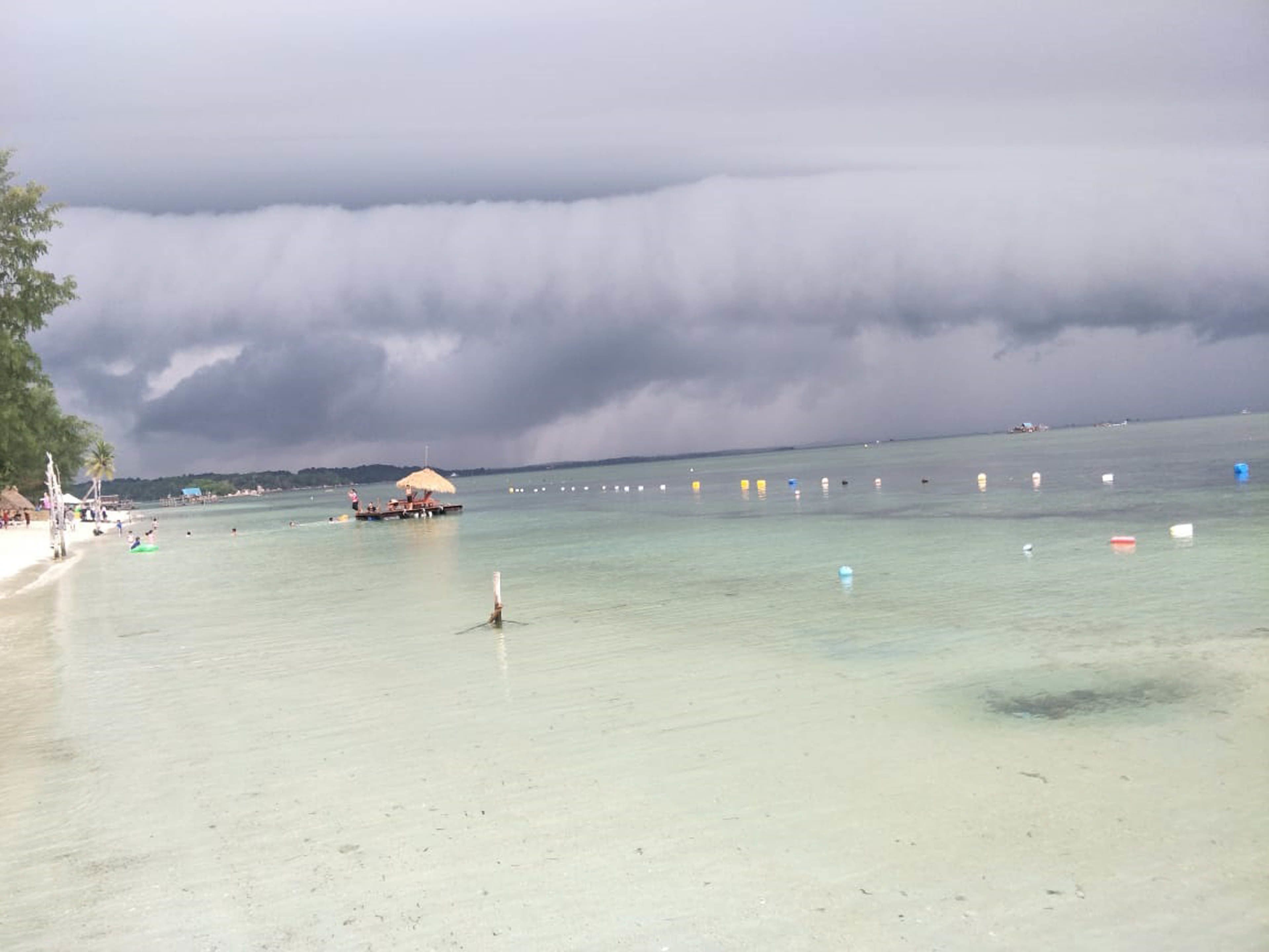 A beach with clear water, a boat, and a thatched-roof structure.