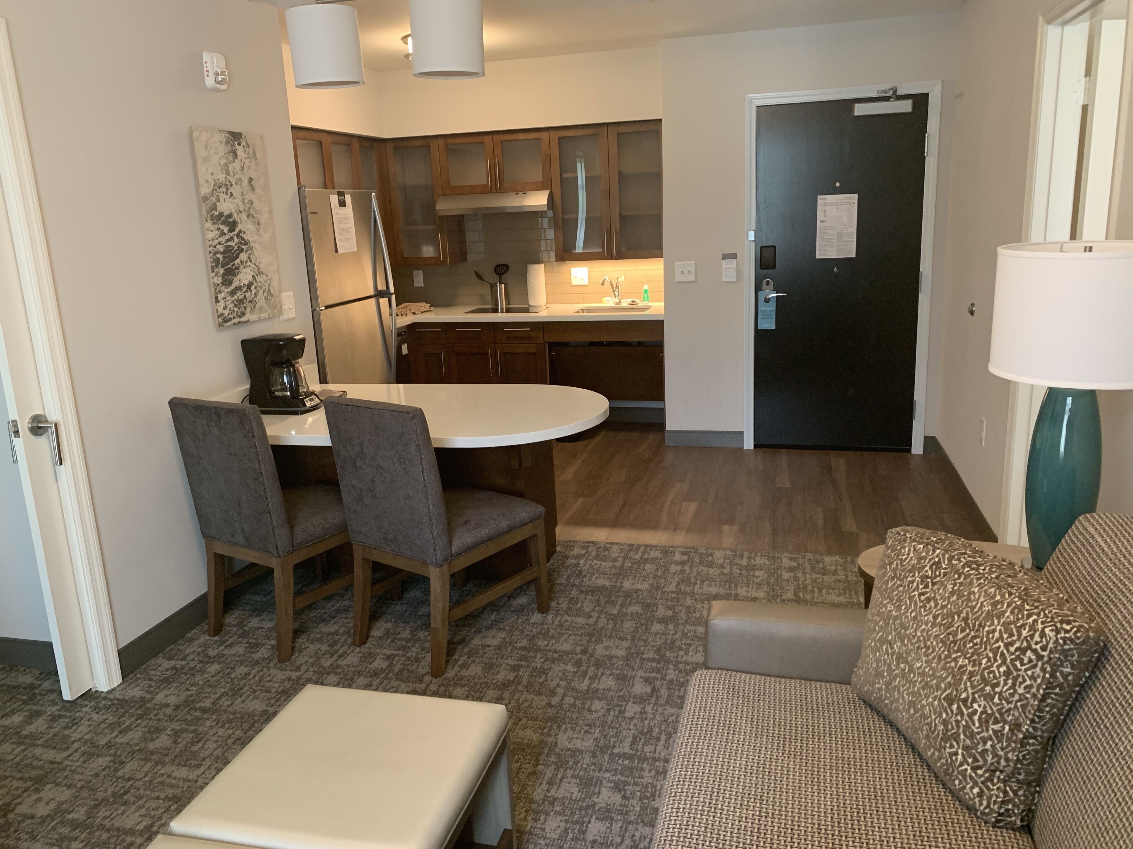 A compact living space with a kitchenette, a dining area with a table and chairs, a sofa, and a lamp.