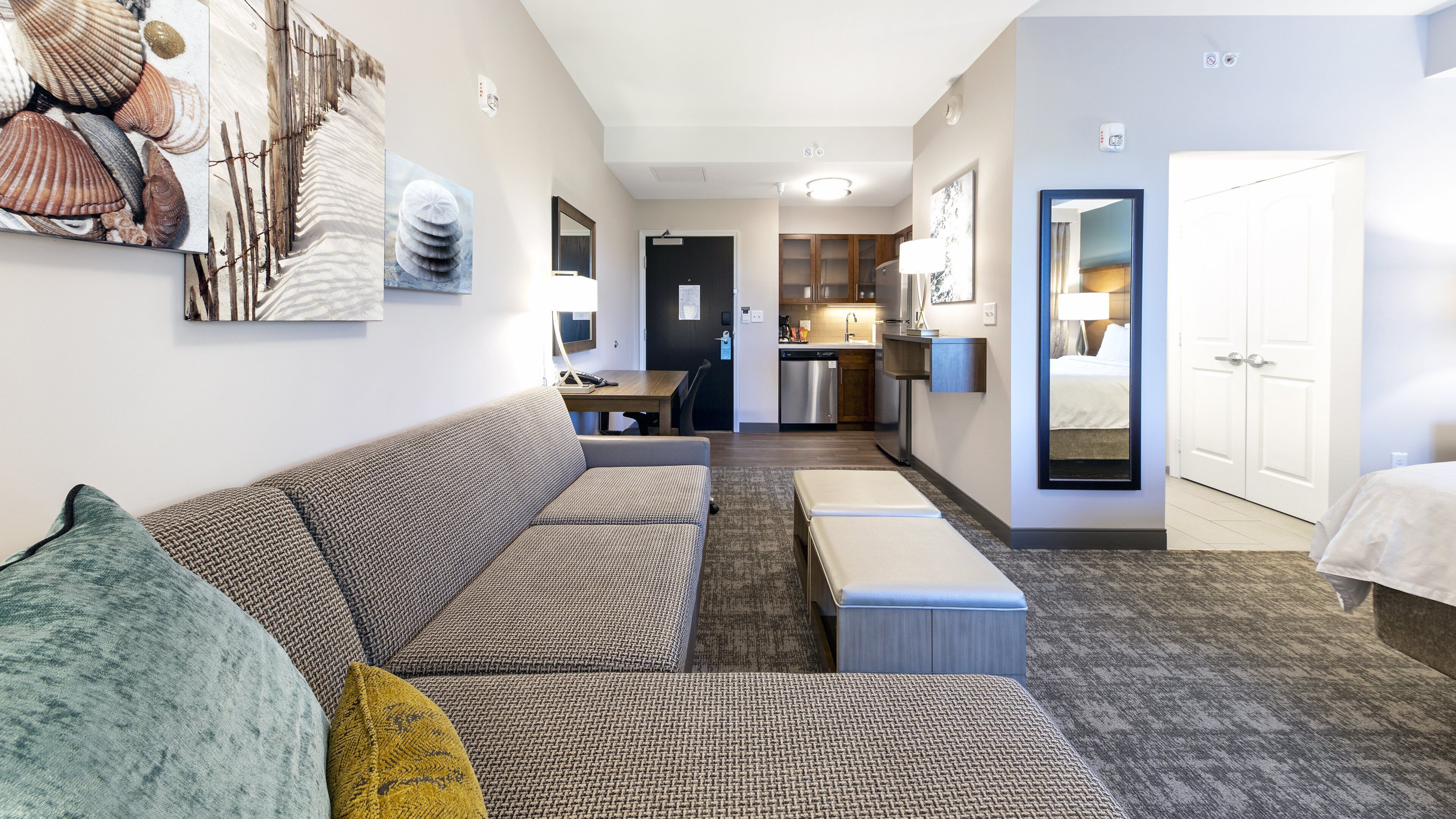 A modern hotel room with a sofa, a small table, a kitchenette, and a bathroom.