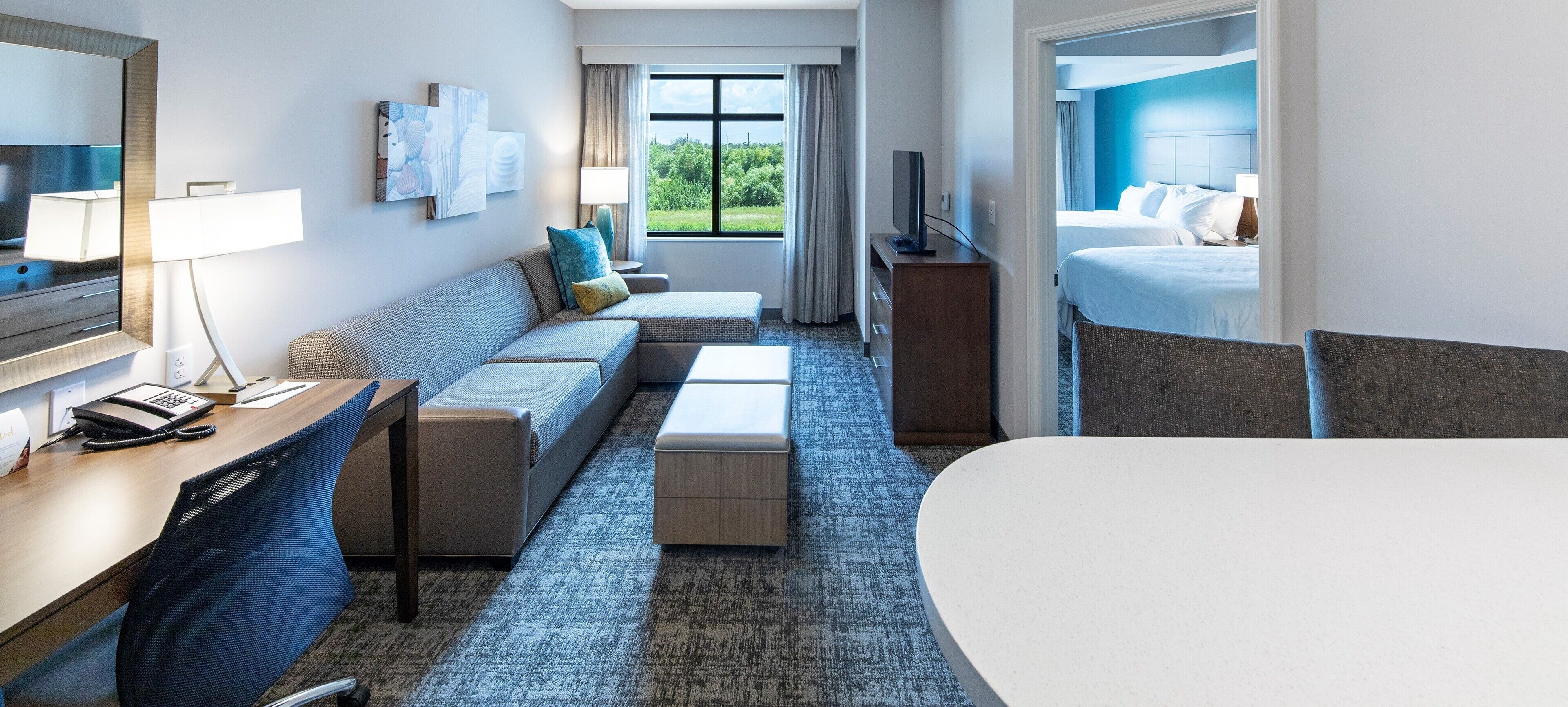 Habitación de hotel con sofá, escritorio con teléfono, televisión, cama y vista a zonas verdes.