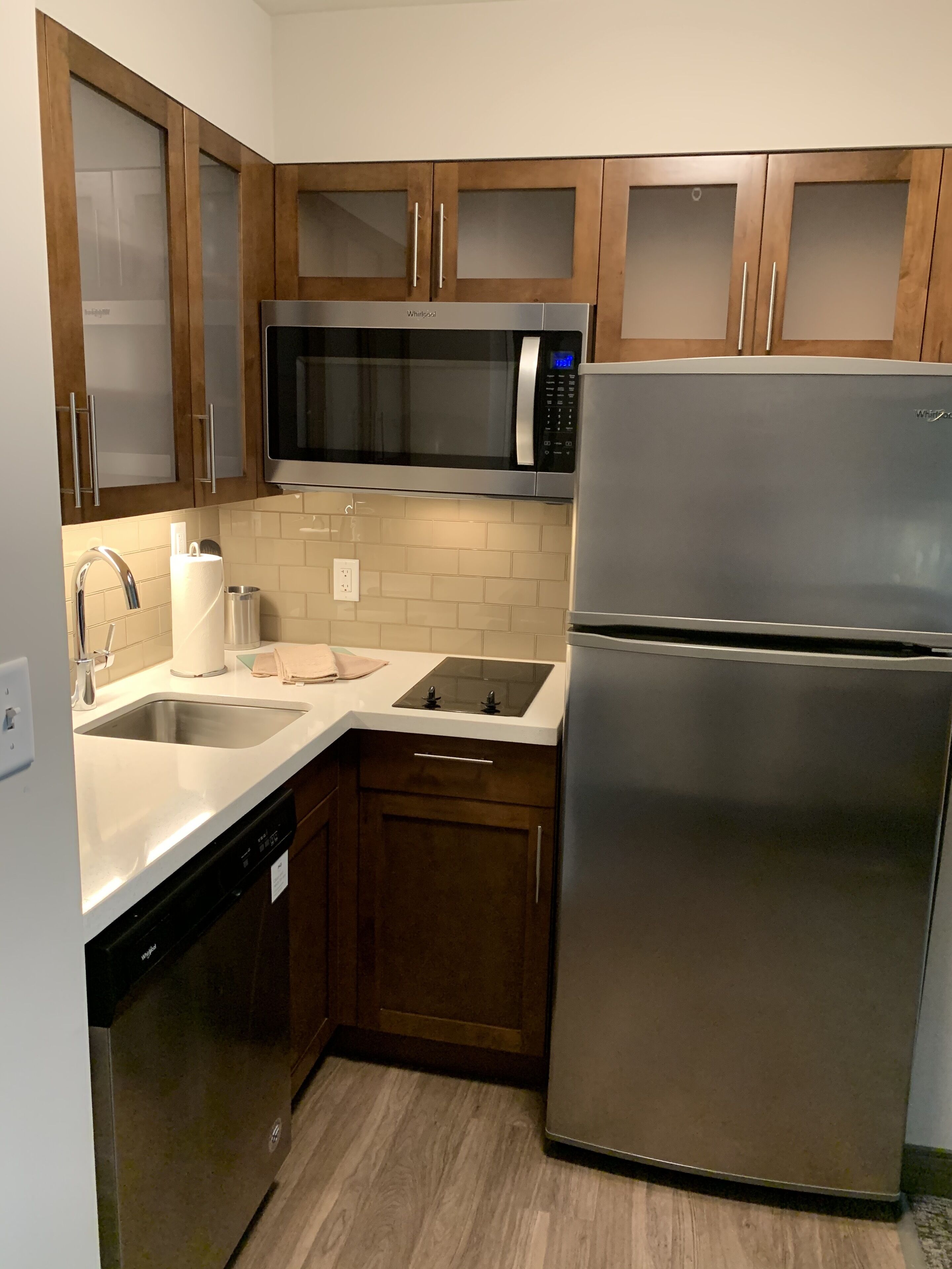 Una cucina compatta con mobili in legno, un forno a microonde in acciaio inossidabile, un frigorifero, un lavello e una lavastoviglie.