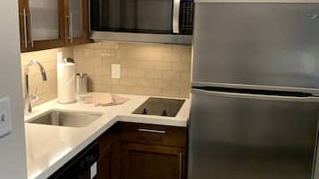 A compact kitchen with wooden cabinets, a stainless steel microwave, a refrigerator, a sink, and a dishwasher.