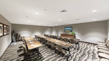 Un salón de conferencias con una larga mesa, sillas, una pantalla de televisión y una alfombra estampada.