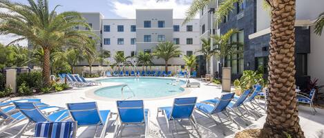 A pool area with blue lounge chairs and palm trees.