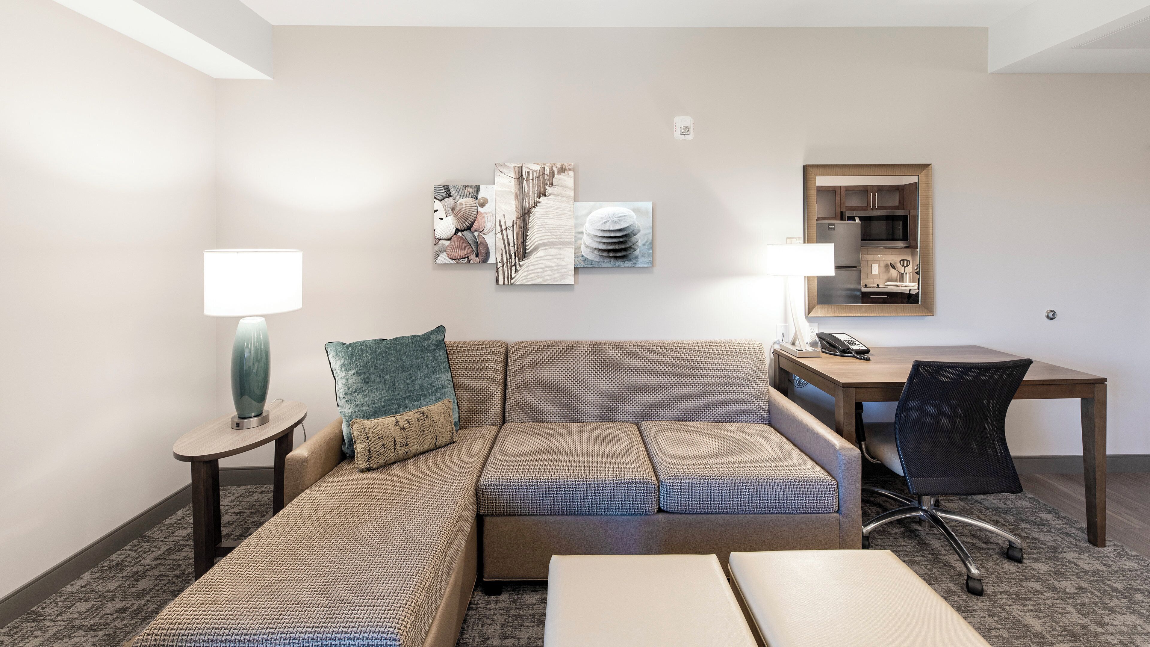 A hotel room with a sofa, two side tables, a desk, a chair, and artwork on the wall.