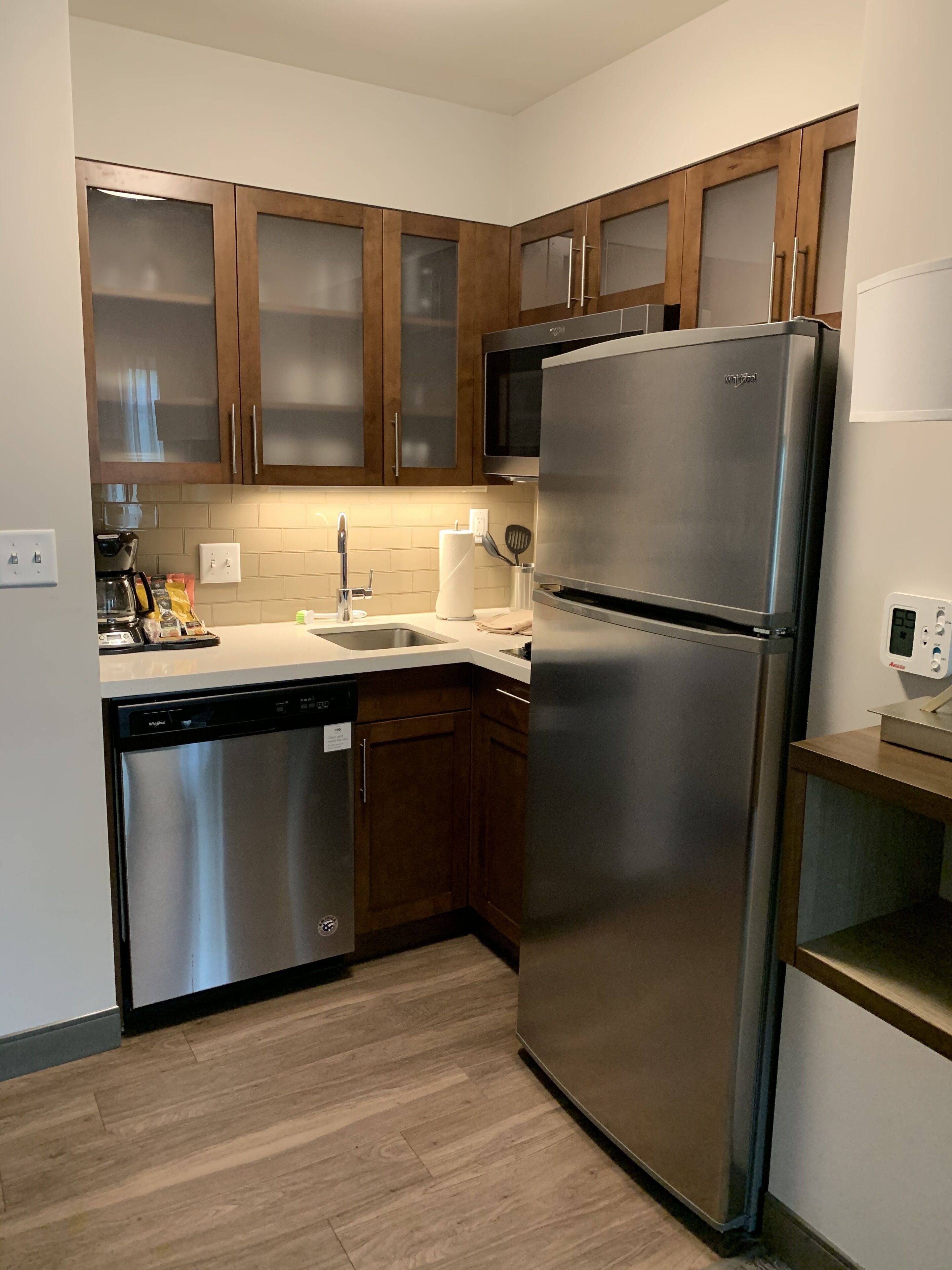 A modern kitchen with wooden cabinets, a stainless steel refrigerator, a dishwasher, and a microwave.