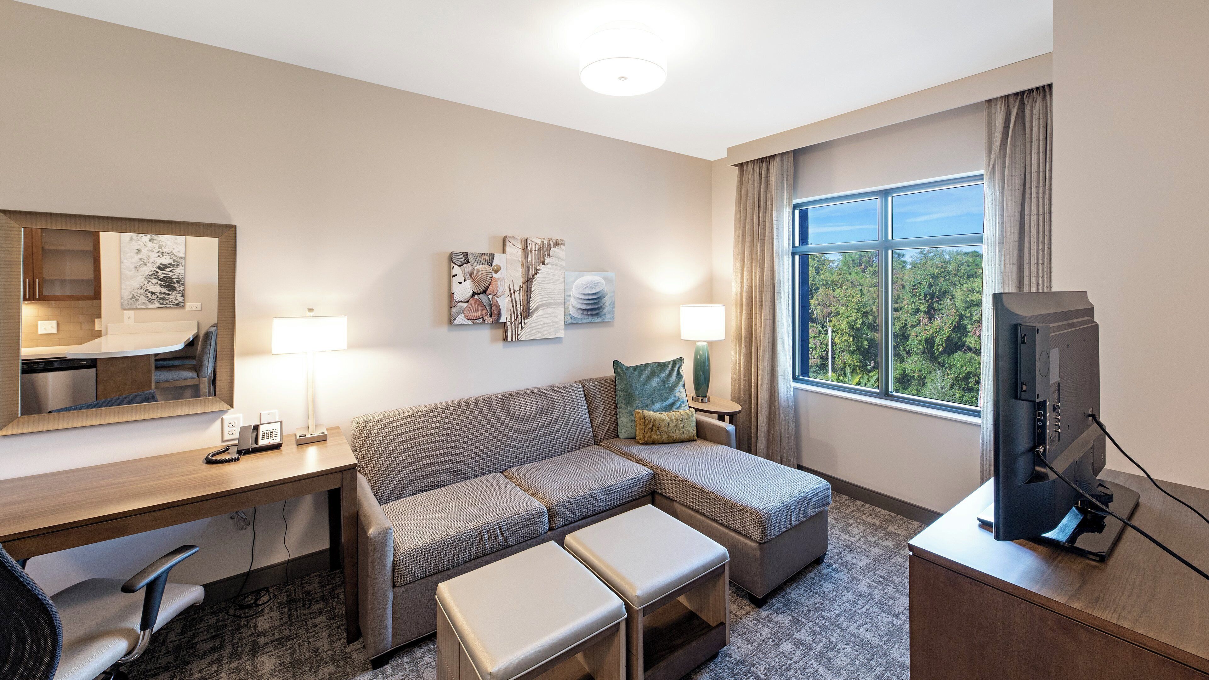A hotel room with a sofa, a desk, a television, and artwork on the walls.