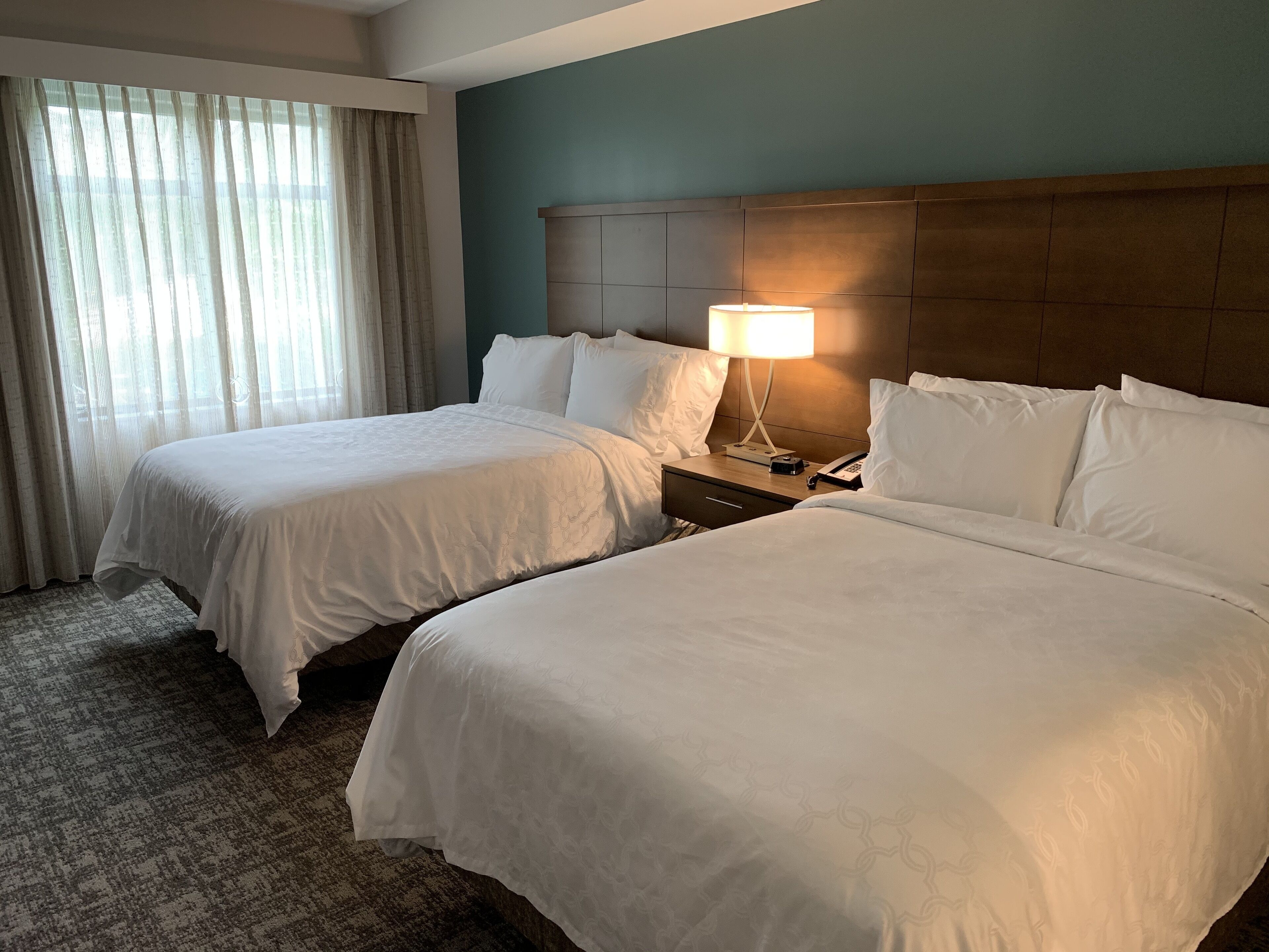 Une chambre d’hôtel avec deux lits, une table de chevet avec une lampe et une fenêtre avec des rideaux.