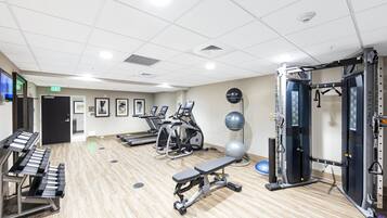 Un gimnasio con cintas de correr, elípticas, prensa de banca y una jaula para sentadillas.