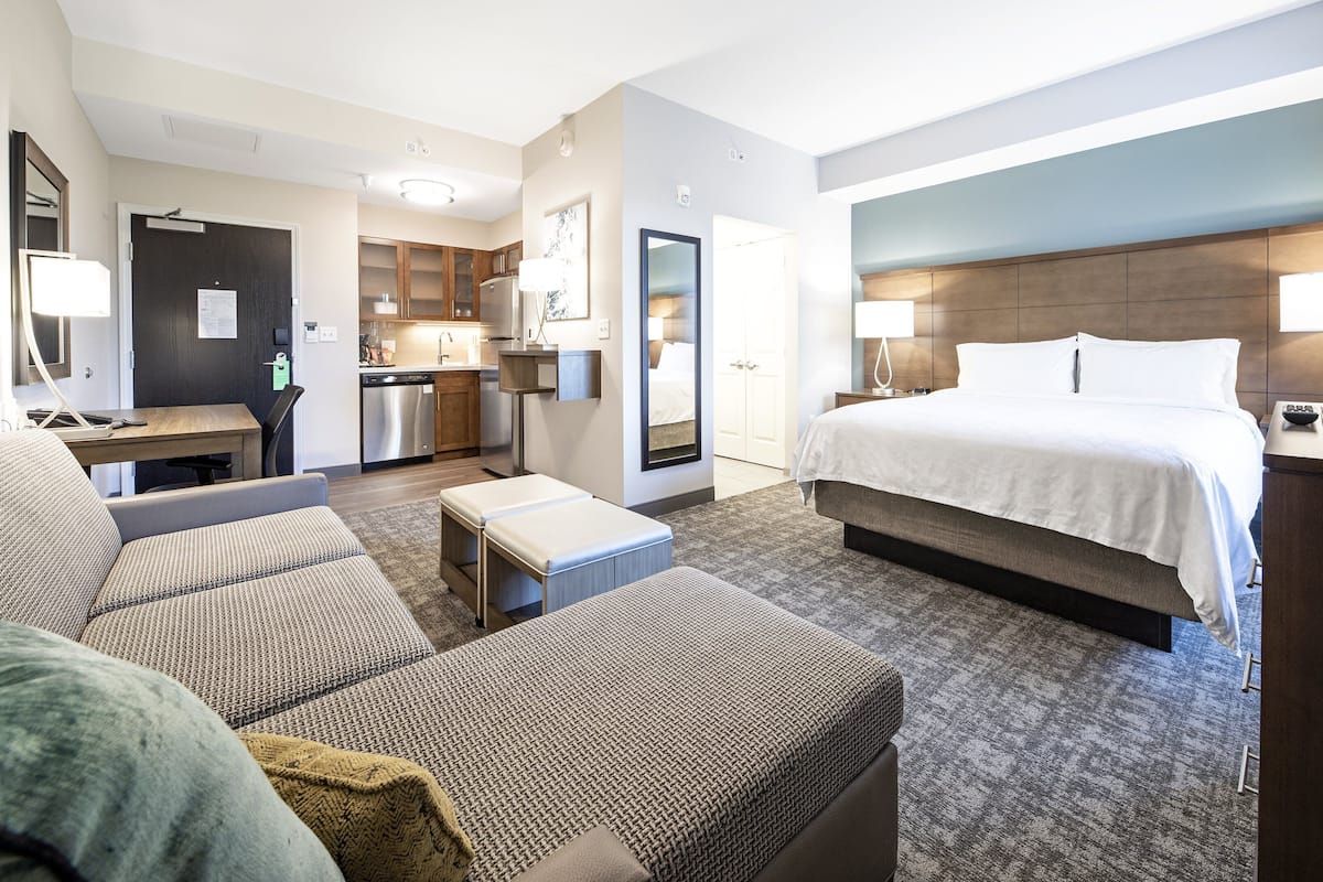 A hotel room with a bed, a sofa, a desk, and a kitchenette.