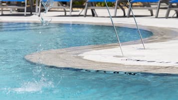 A pool with clear water, a diving board, and blue lounge chairs in the background.