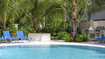 A swimming pool with blue lounge chairs, palm trees, and a barbecue grill.