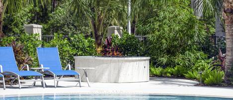 Un área de piscina con sillones reclinables azules y una jardinera de hormigón con plantas.