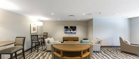 A hotel room with a large sofa, a wooden coffee table, a TV mounted on the wall, and a patterned carpet.