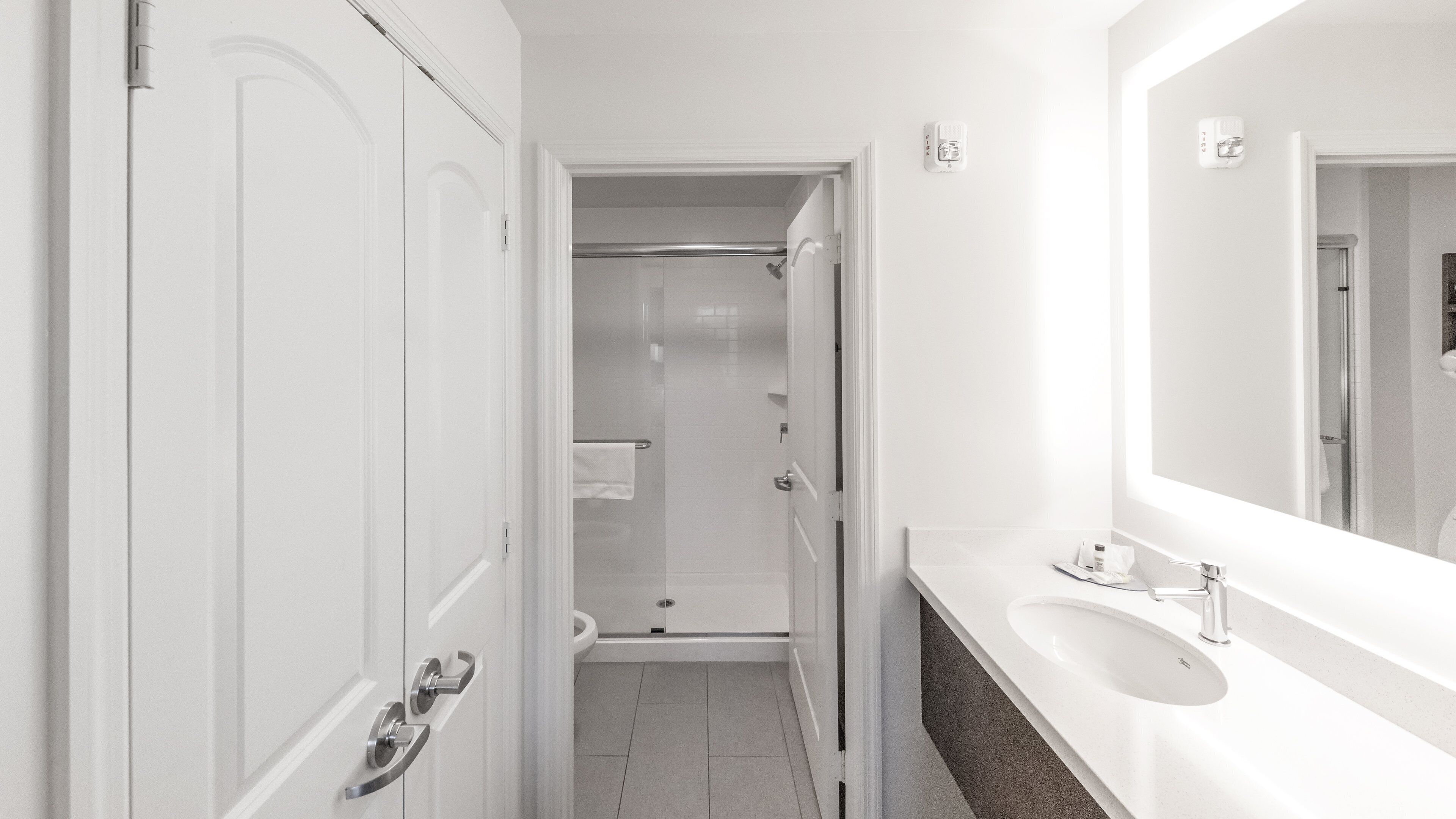 Een kleine, witte badkamer met een douche, wastafel en spiegel.