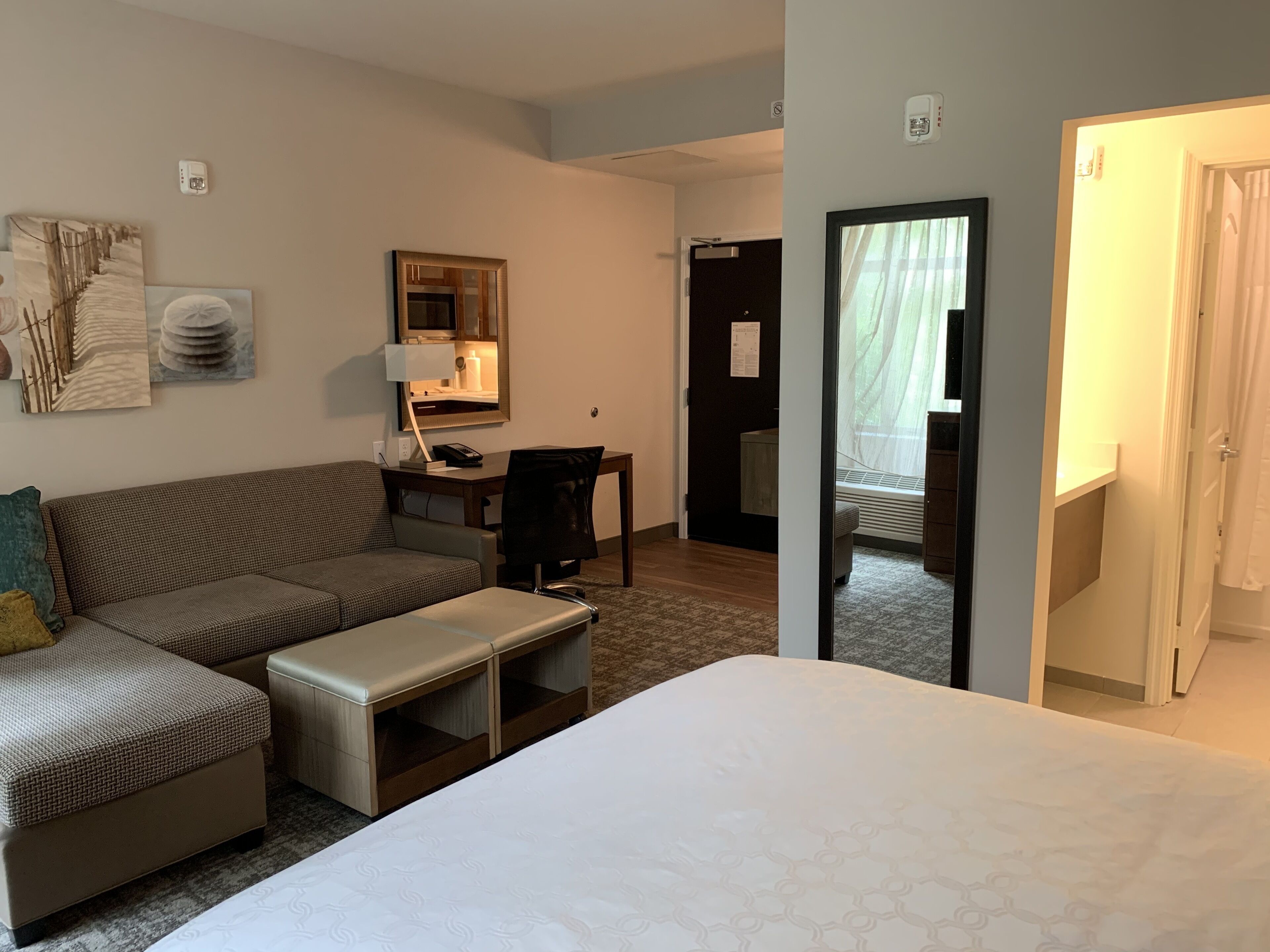 Habitación de hotel con cama, sofá, escritorio con silla, espejo y puerta que da a otra habitación.