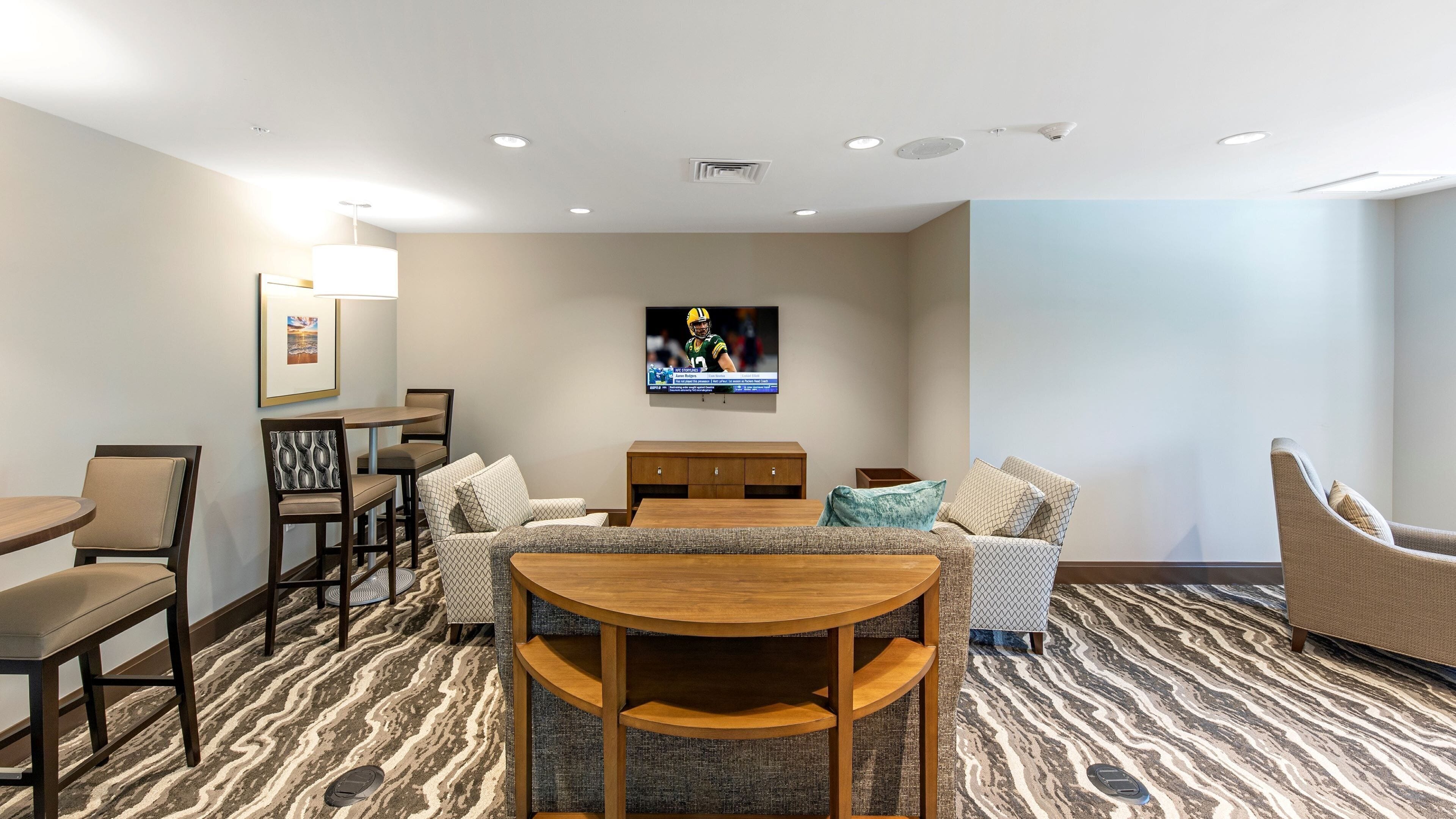 A hotel room with a dining area, a TV mounted on the wall, and a patterned carpet.