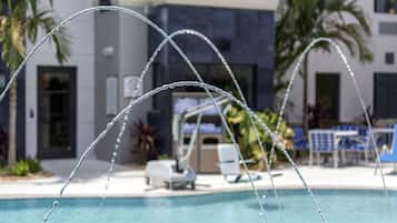 Una piscina amb jato d'aigua, gandules i un edifici modern al fons.