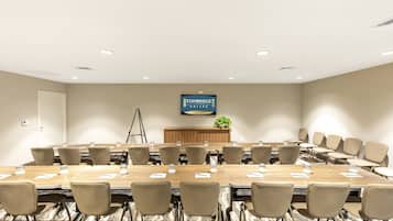 A conference room with a long table, multiple chairs, a television screen, and a plant on a wooden cabinet.