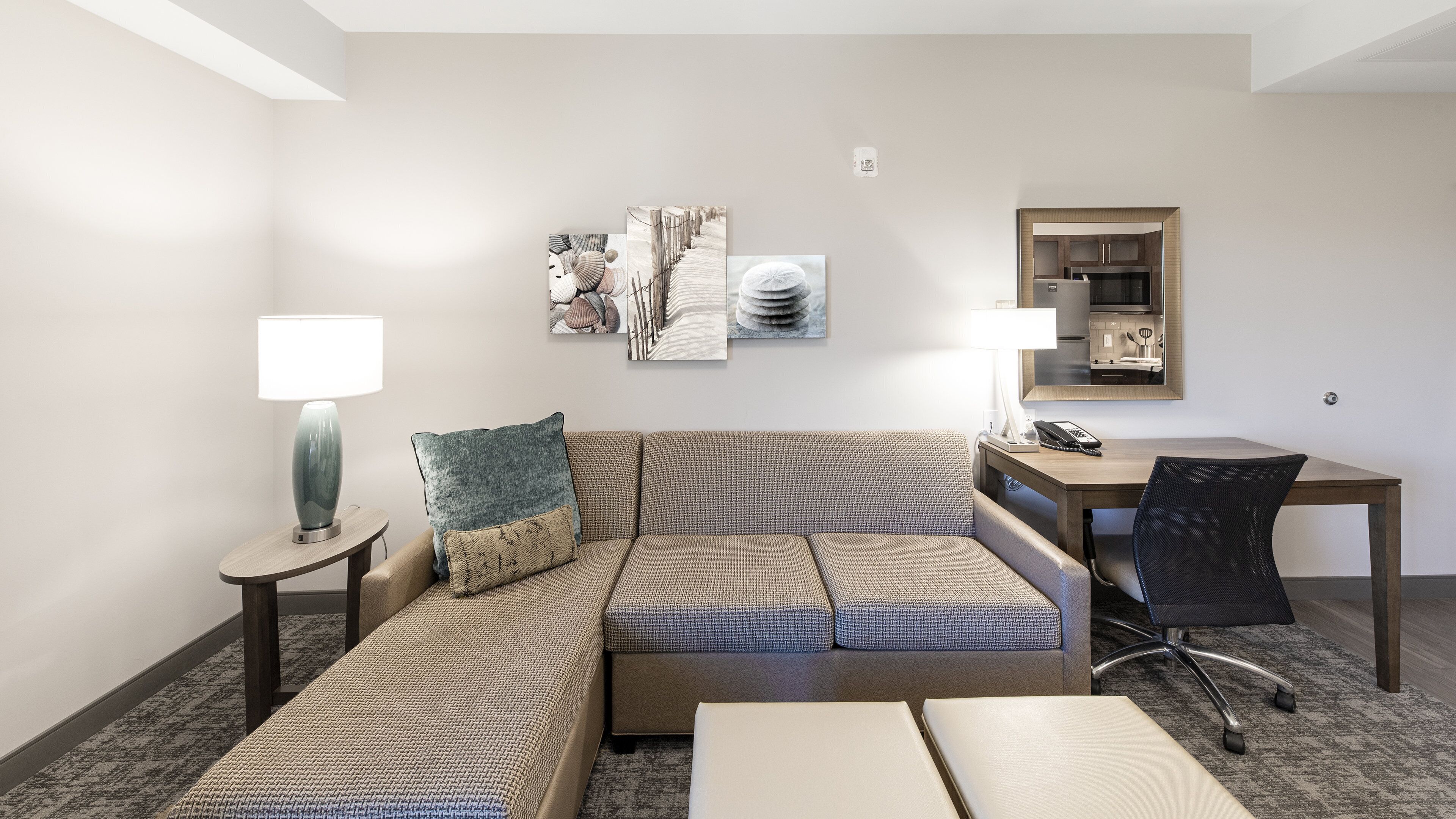 A hotel room with a sofa, two side tables, a desk, a chair, and artwork on the wall.